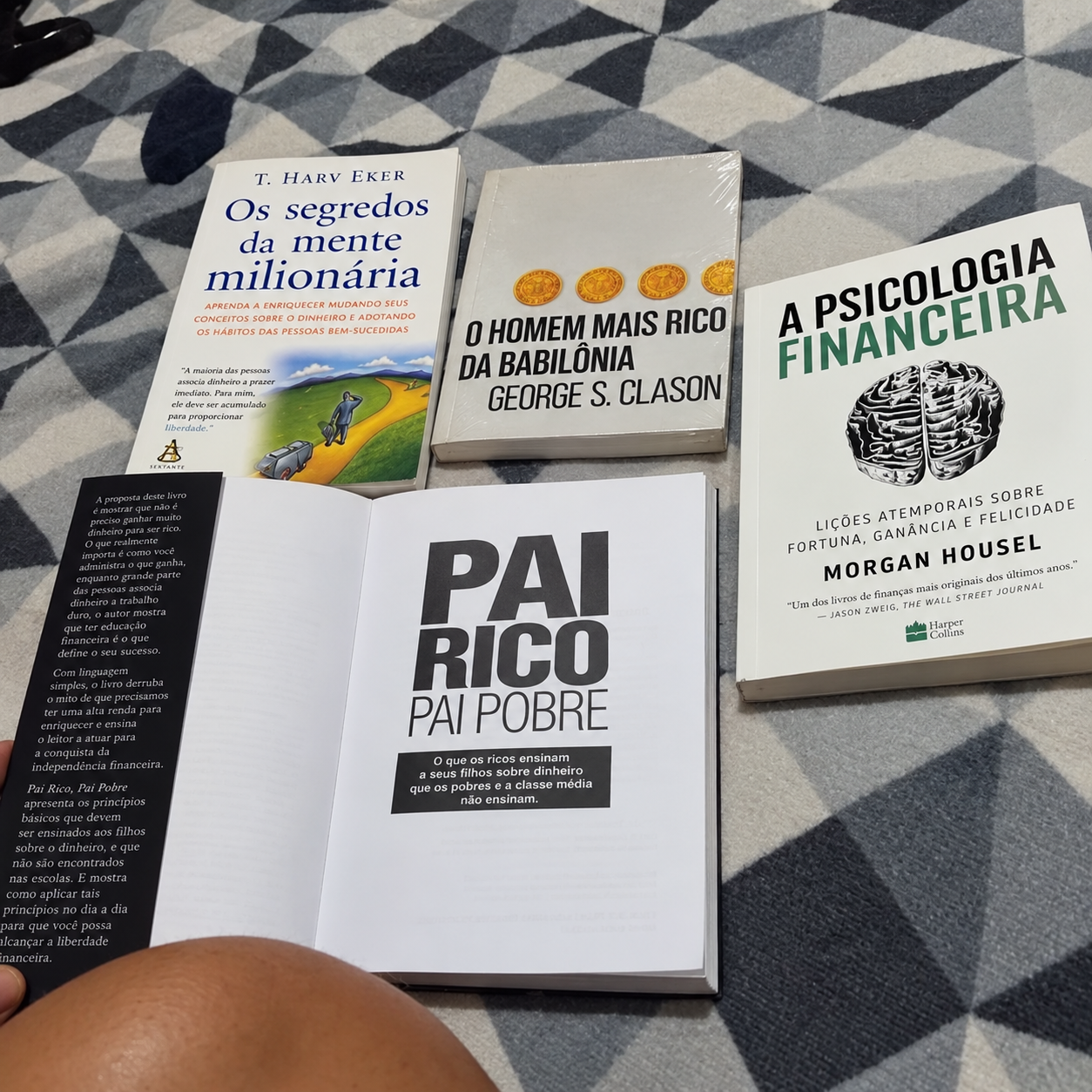 Livros do kit de educação financeira sobre uma cama, com Pai Rico, Pai Pobre aberto