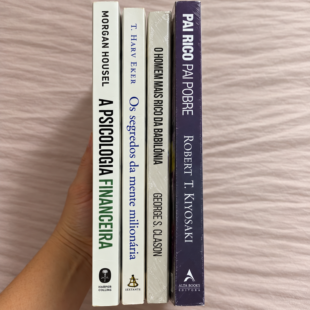 Lombadas dos quatro livros de educação financeira seguradas em uma mão